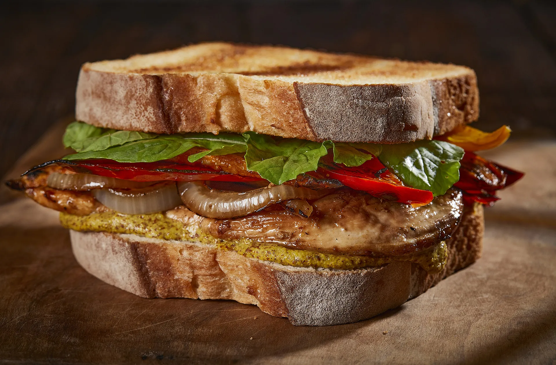 Sándwich de pollo a la brasa con mostaza Dijon, cebolla caramelizada, pimiento y rúcula