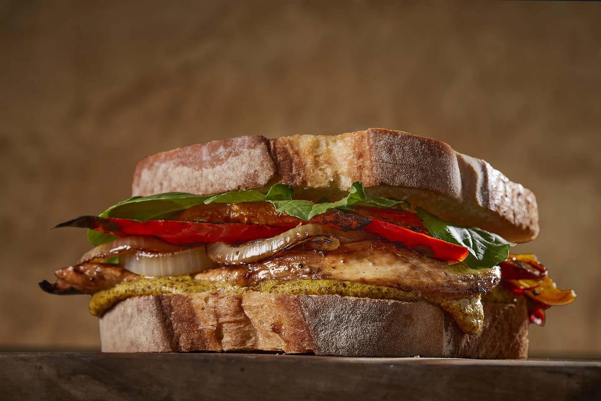 Sándwich de pollo a la brasa con mostaza Dijon, cebolla caramelizada, pimiento y rúcula